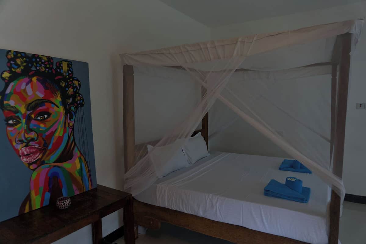 A room with a bed under a canopy, a painting on the wall, and a small table.