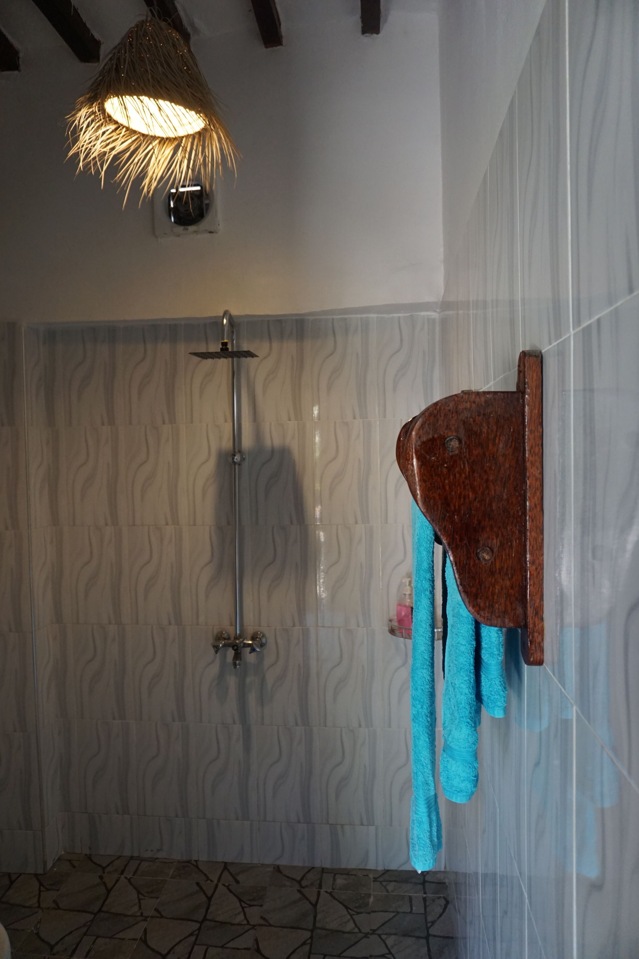 A bathroom with a shower, a towel rack with towels, and a textured wall.