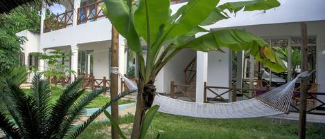 A hammock in a lush garden area with a white building in the background.