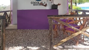Zona de recepción de una casa de playa, con un logotipo, un hombre en un atril y asientos al aire libre.