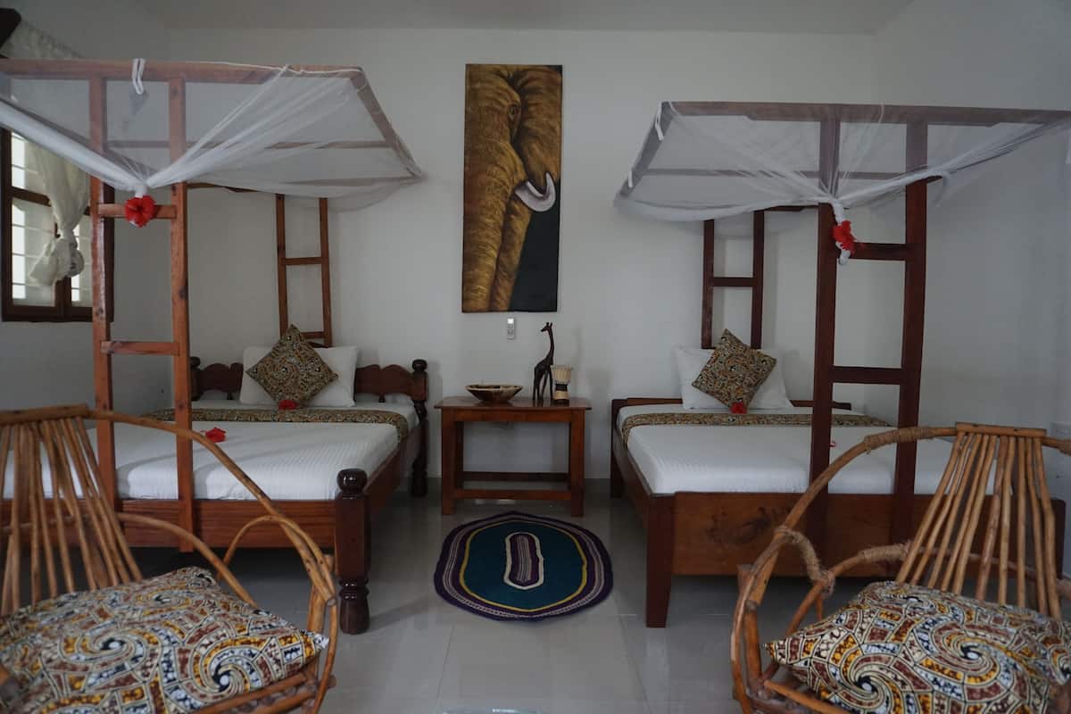 A room with two wooden beds, each with a canopy, and a small table with a bowl and a lamp.