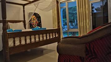 Una habitación con una cama con dosel, una ventana con cortinas y un sofá estampado.