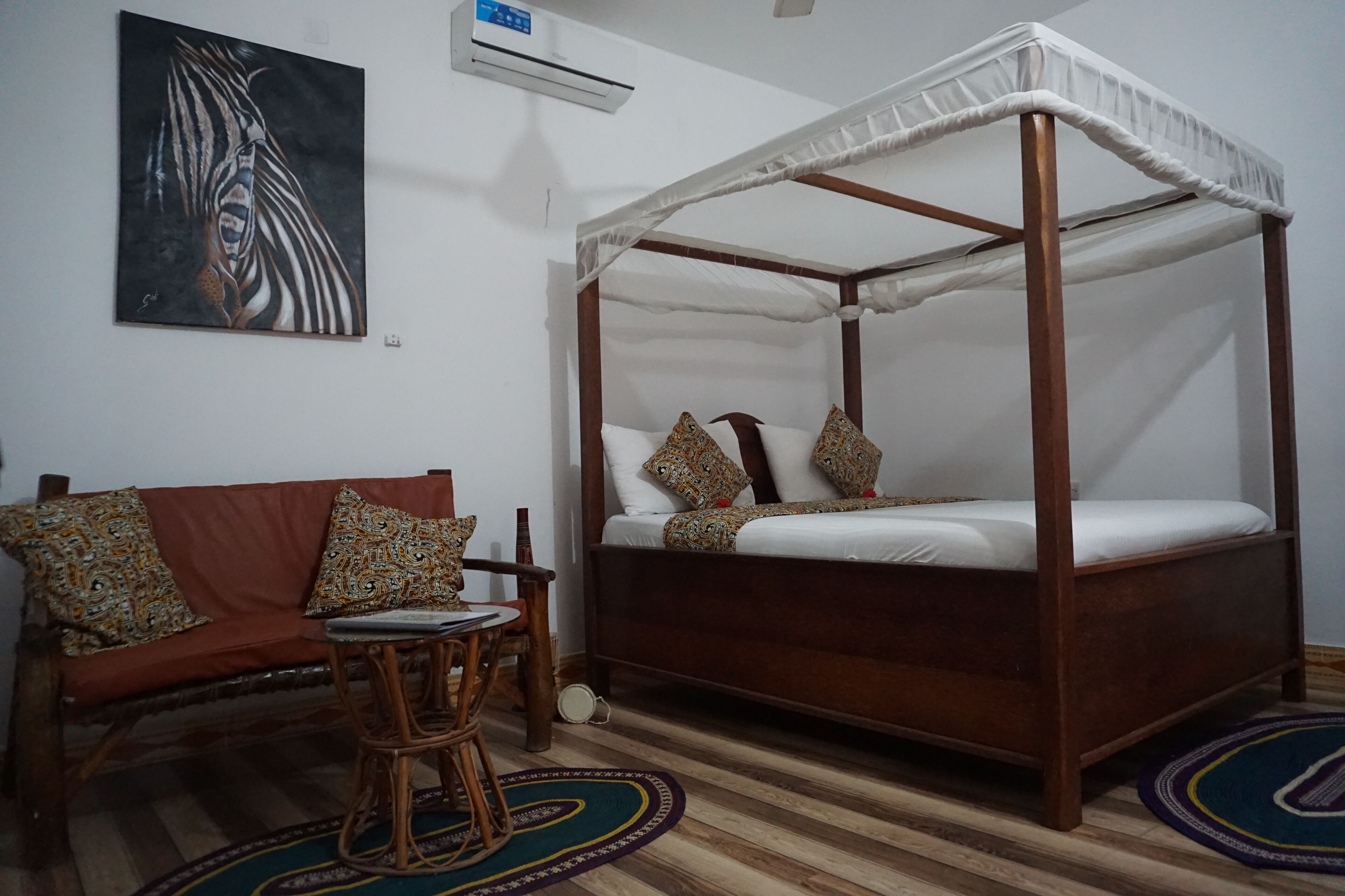 A room with a four-poster bed, a sofa with patterned cushions, a small round table, and a colorful rug.