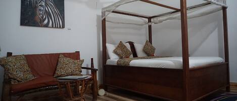 A room with a four-poster bed, a sofa with patterned cushions, a small round table, and a colorful rug.