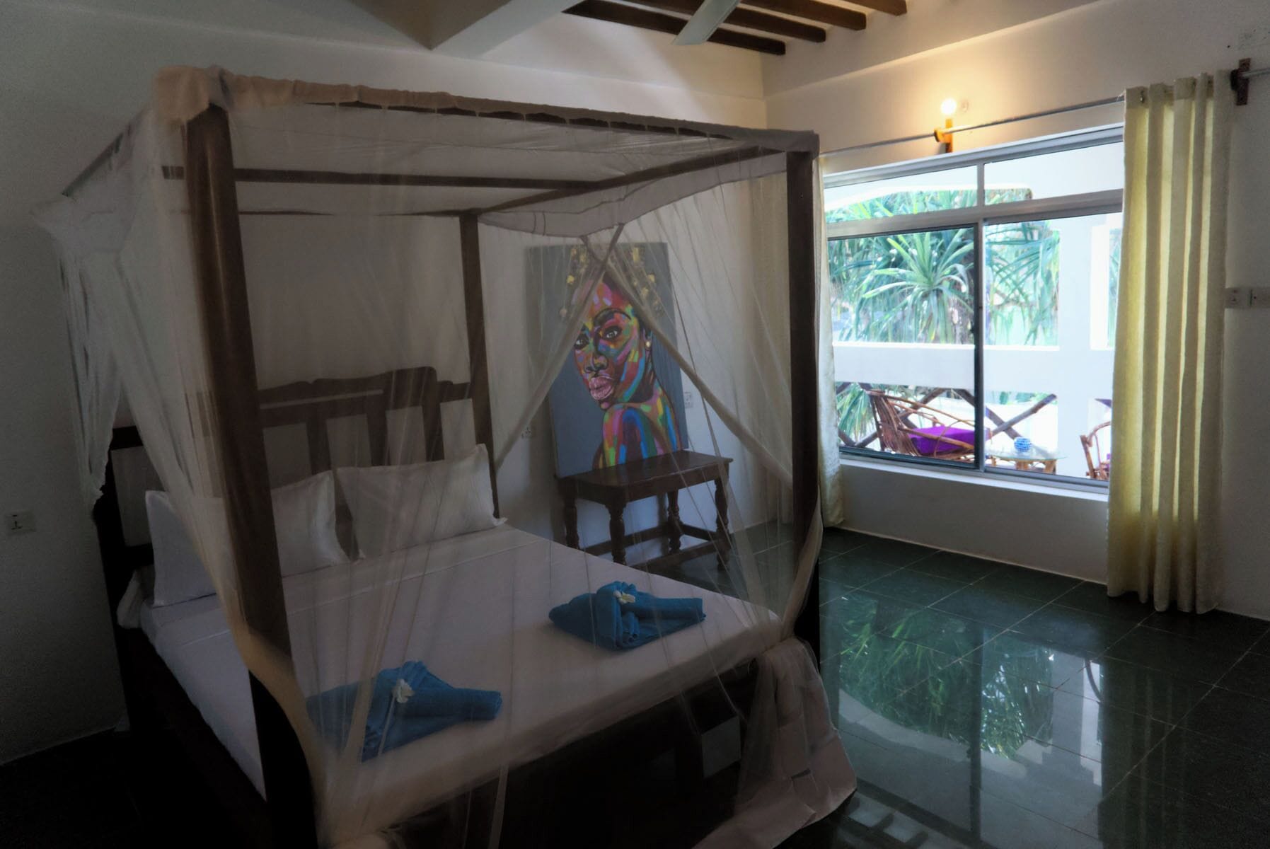 A room with a four-poster bed, a small table, and a painting on the wall.