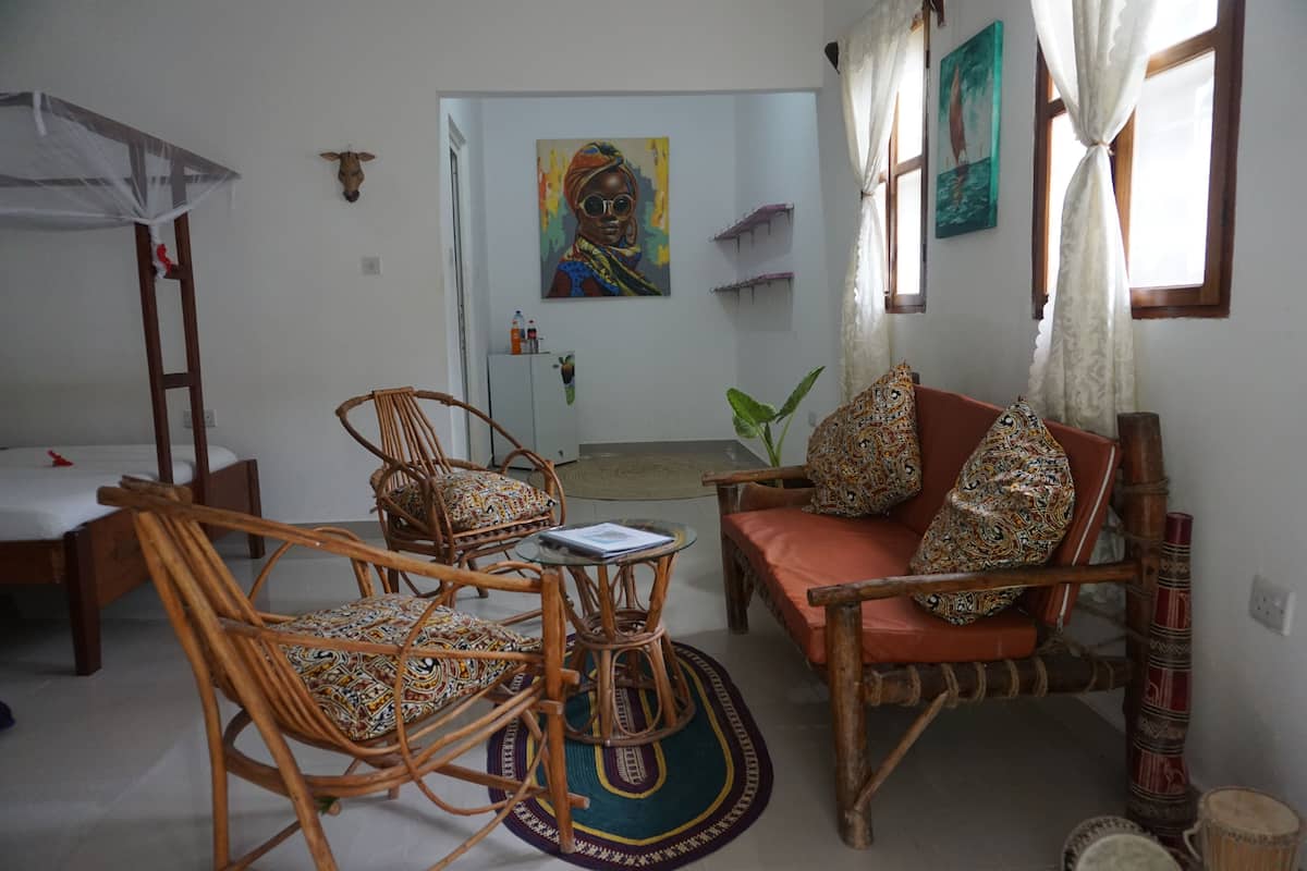 A room with a bed, a sofa, two rocking chairs, a small table, and a door leading to another room.