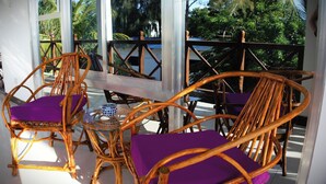 Un espacio de estar techado al aire libre con sillas de mimbre y cojines morados, con vistas a un jardín exuberante.