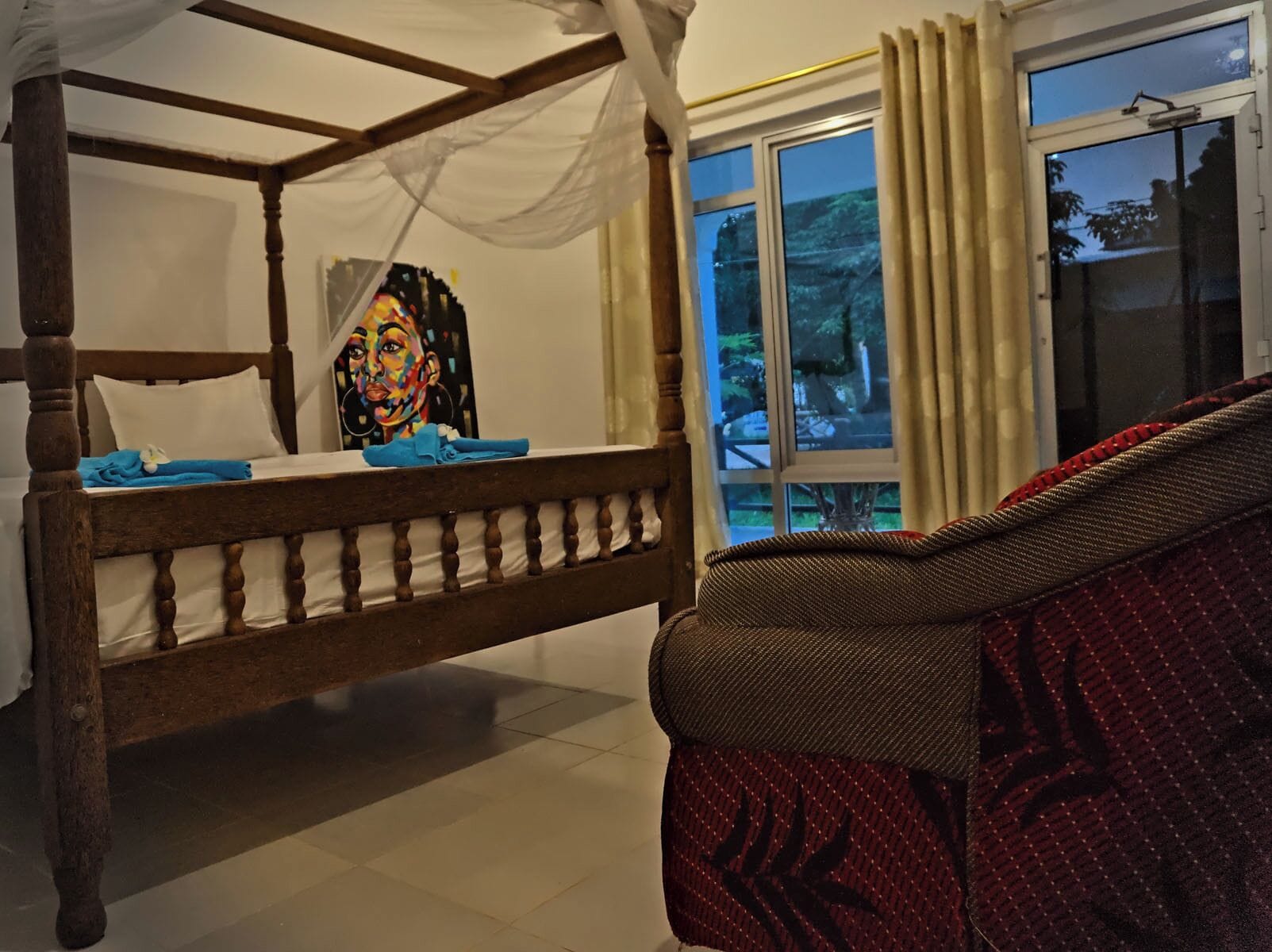 A room with a four-poster bed, a window with curtains, and a patterned sofa.