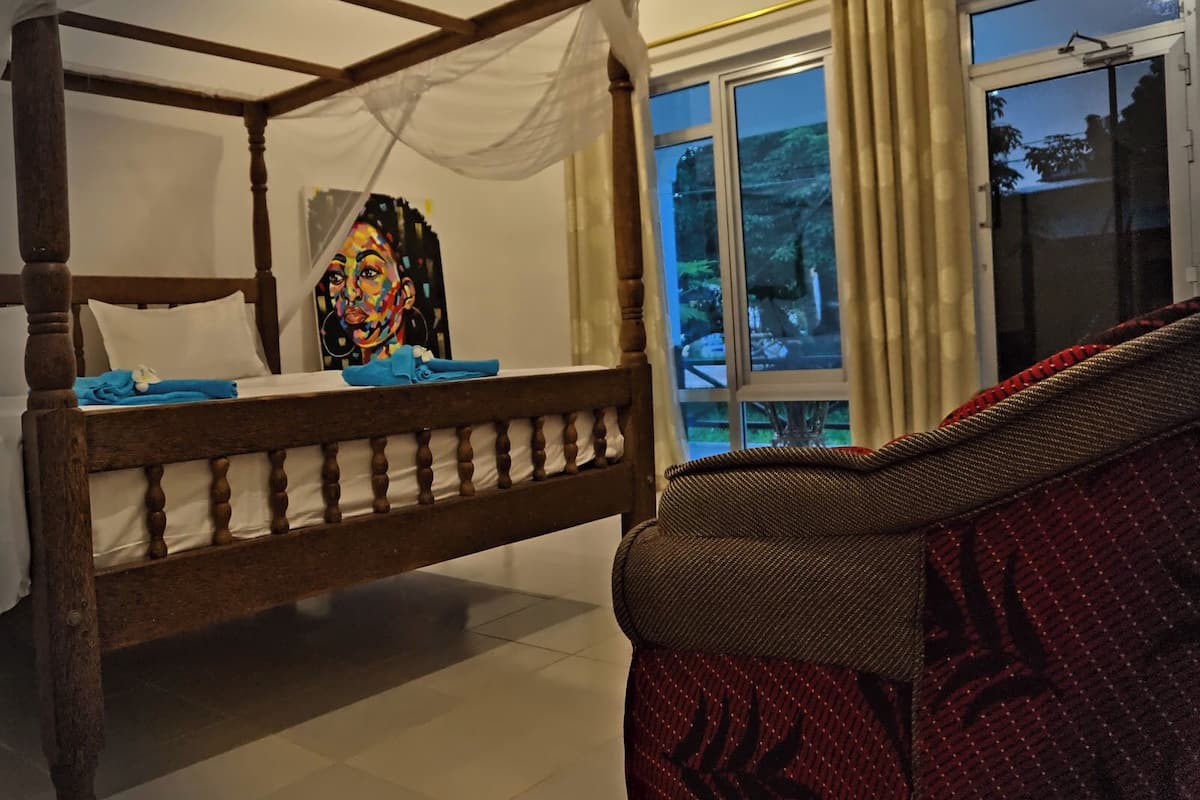 A room with a four-poster bed, a window with curtains, and a patterned sofa.