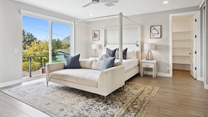 A bedroom with a four-poster bed, a ceiling fan, and a large window with a view of trees. - Lavish Luxuries-Pool/Spa, Games, Walk To Old Town! (Scottsdale)