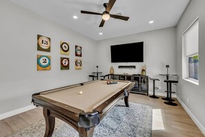 A pool table with a ceiling fan, a television, and a bar area with stools.
