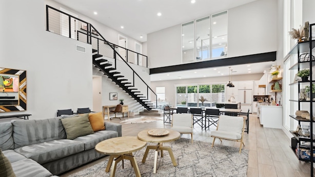 A spacious living area with a grey sectional sofa, a staircase, and a kitchen in the background. - Lavish Luxuries-Pool/Spa, Games, Walk To Old Town! (Scottsdale)