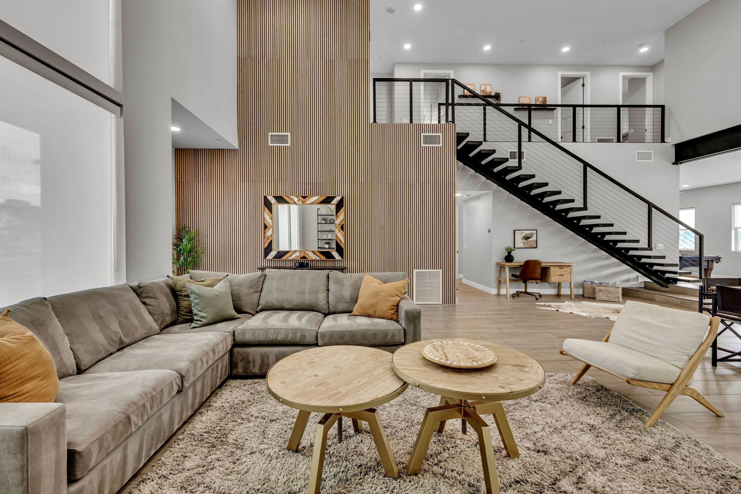 A spacious living area with a sectional sofa, two round coffee tables, and a staircase leading to an upper level.