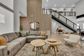 A spacious living area with a sectional sofa, two round coffee tables, and a staircase leading to an upper level.