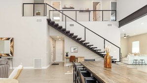 A spacious living area with a wooden dining table, a staircase, and a view of the upper floor. - Lavish Luxuries-Pool/Spa, Games, Walk To Old Town! (Scottsdale)