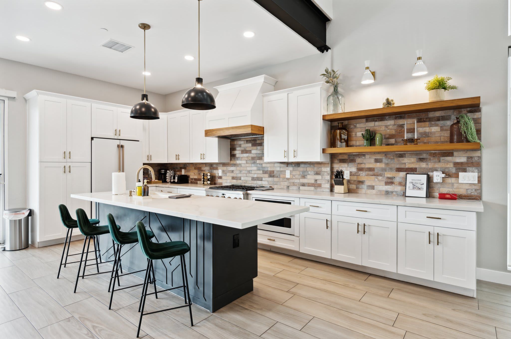 A modern kitchen with white cabinets, a large island with bar stools, a brick backsplash, and pendant lighting.