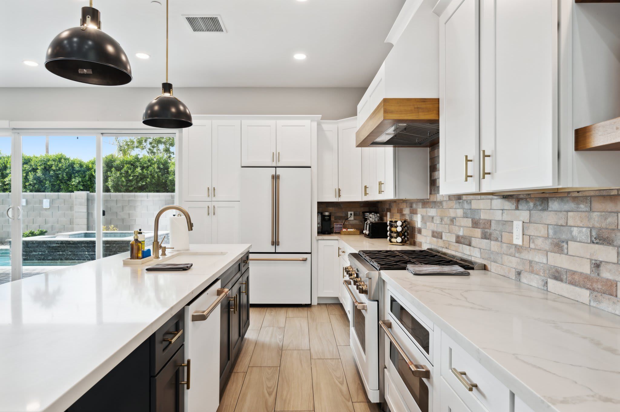 A modern kitchen with white cabinets, a central island, stainless steel appliances, and a view of a swimming pool.