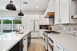 A modern kitchen with white cabinets, a central island, stainless steel appliances, and a view of a swimming pool.
