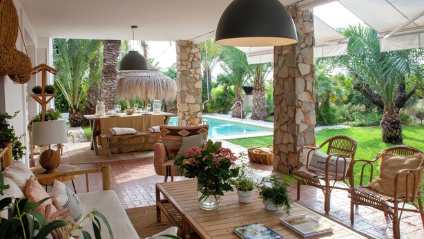 Une terrasse ensoleillée avec une piscine, des meubles en osier et une végétation luxuriante.