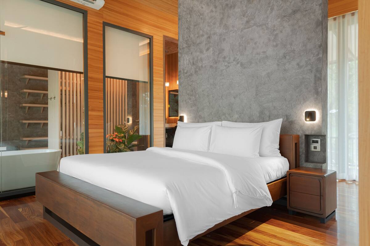 Un dormitorio moderno con una cama grande, suelo de madera, un banco empotrado y una pared gris con textura.
