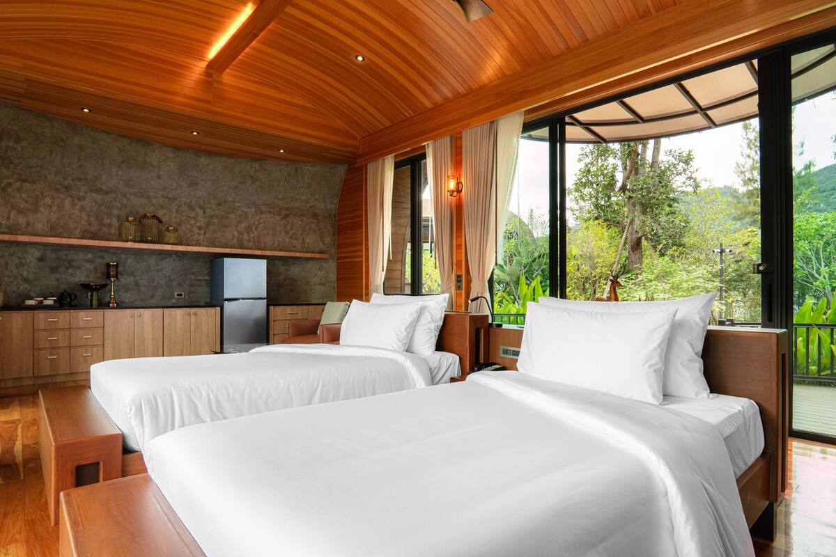 Una habitación de hotel moderna con dos camas, techo de madera, ventanas amplias y una kitchenette.