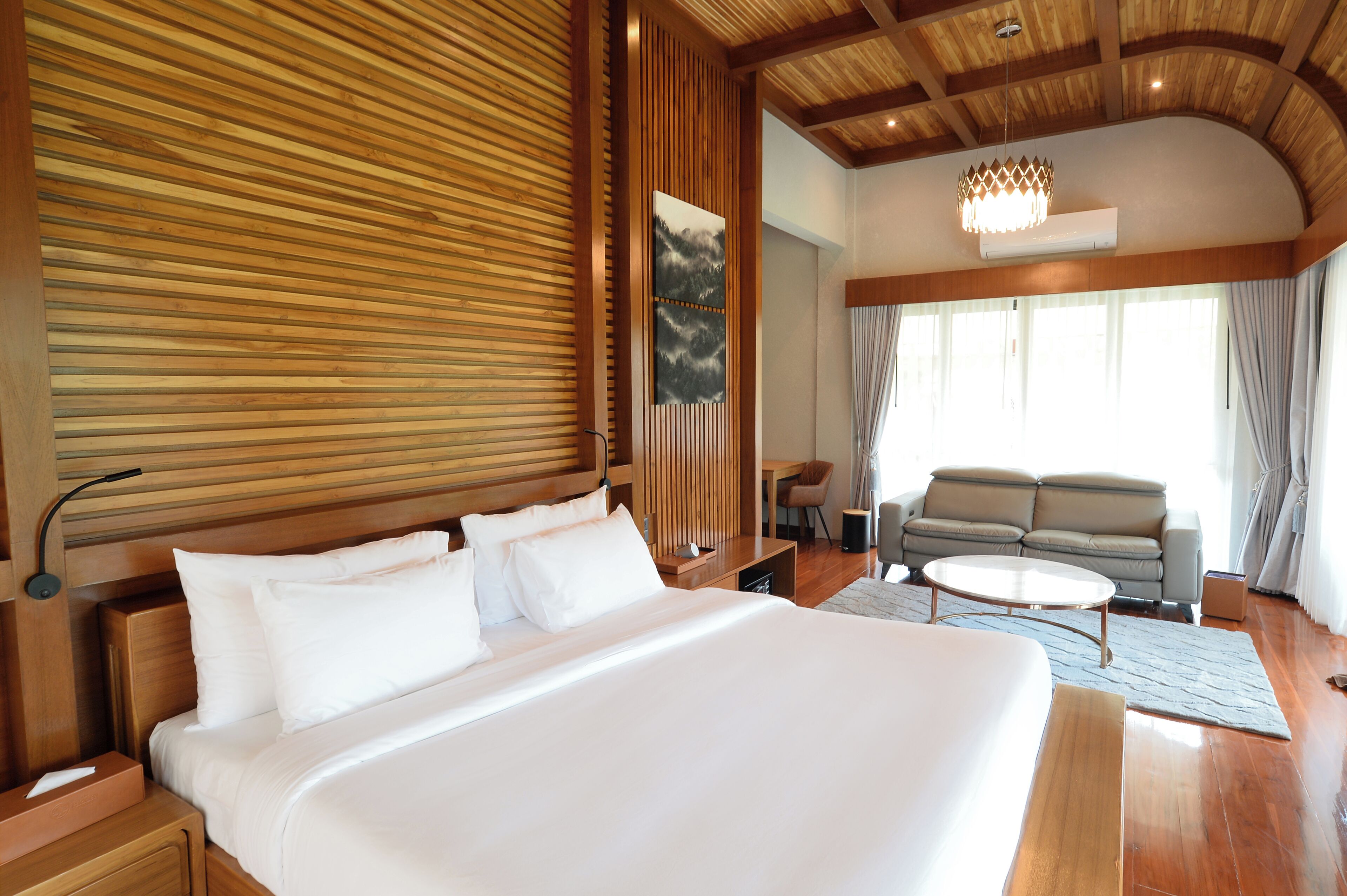 Una habitación de hotel moderna con una cama grande, paneles de madera, un sofá y una mesa de comedor.