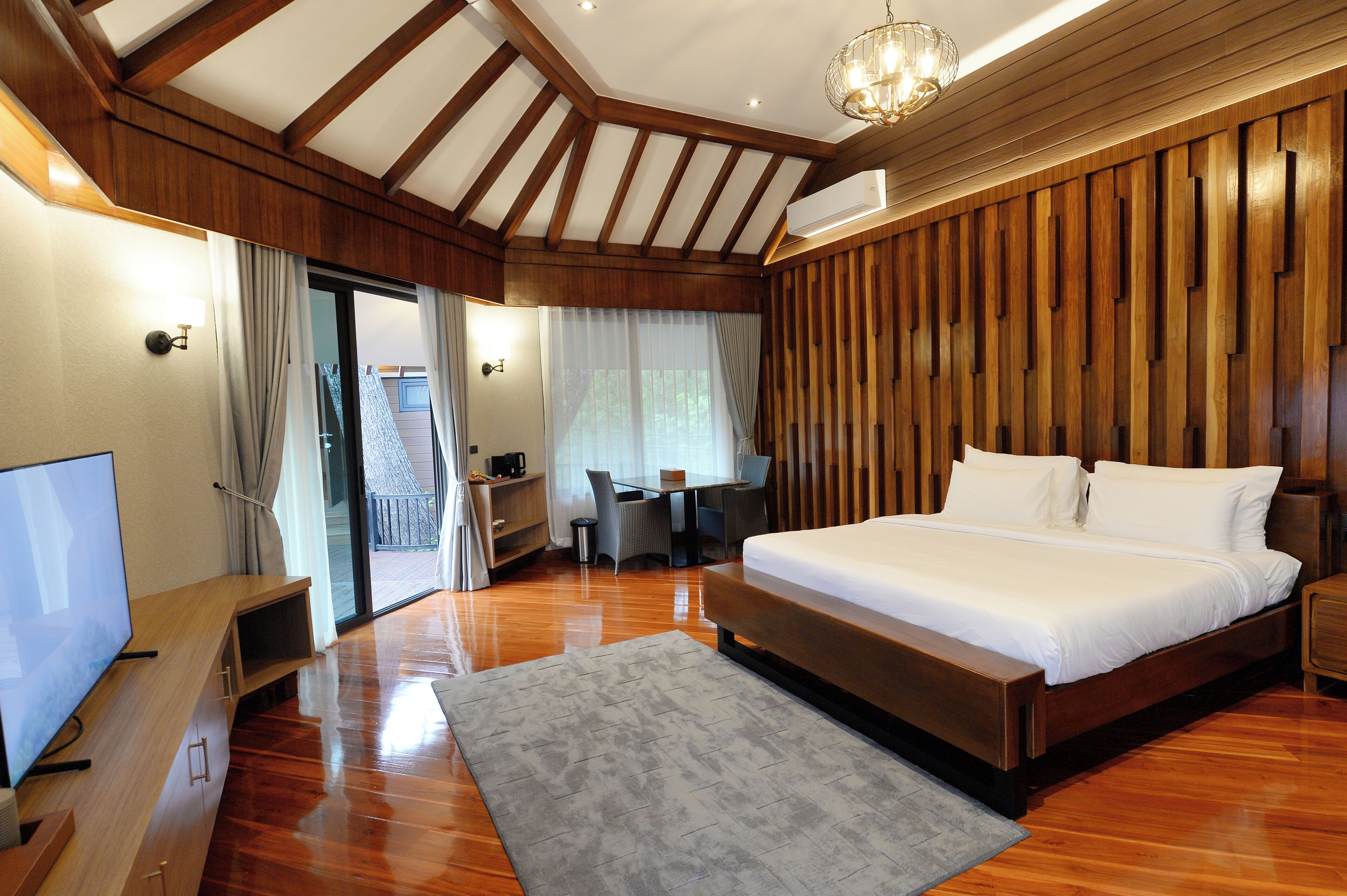 A spacious bedroom with a large bed, wooden paneling, a TV, and a desk area.