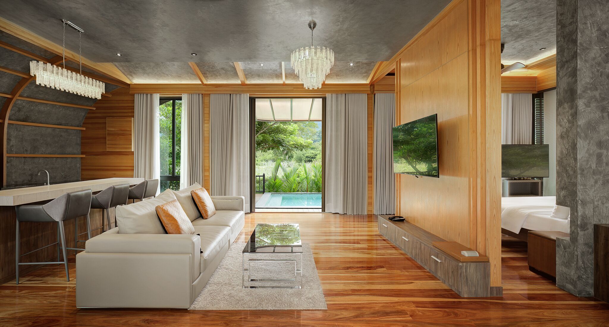 Un salon moderne avec un canapé, une table basse et un téléviseur. On peut apercevoir une piscine à travers la fenêtre.