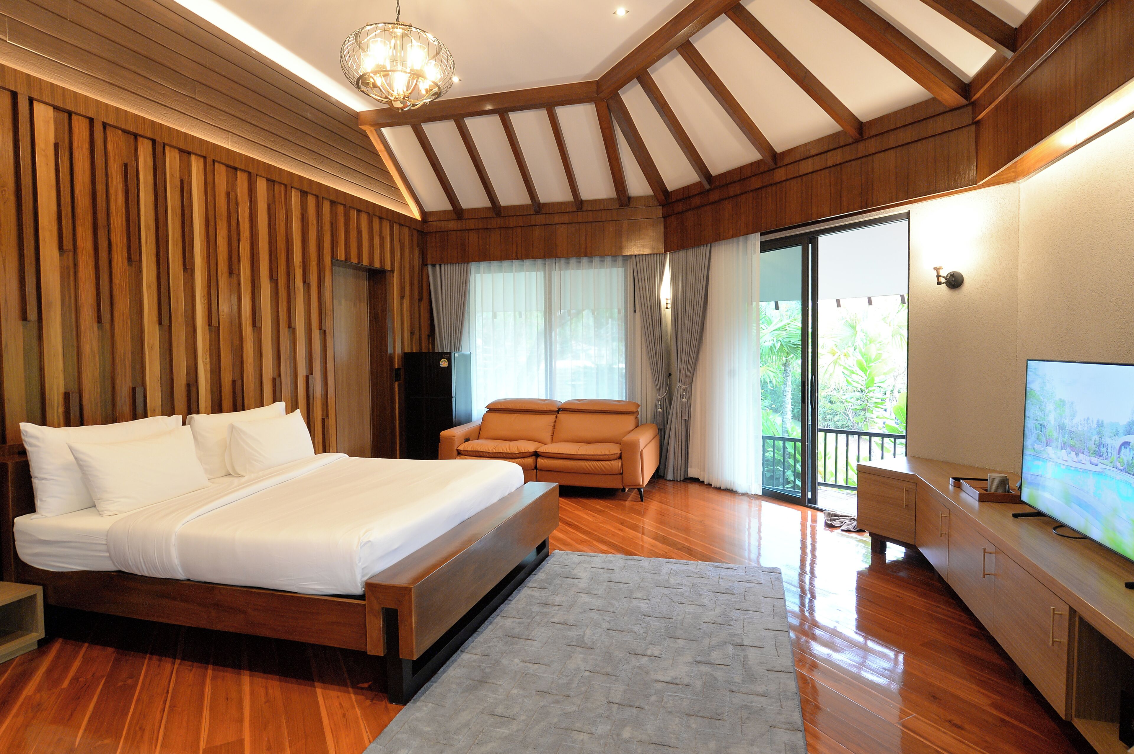 A bedroom with a large bed, a sofa, a TV, and a balcony with curtains.