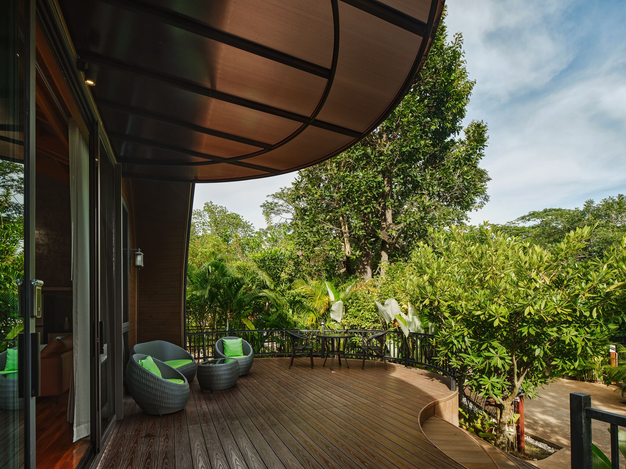 Une terrasse en bois avec des meubles d’extérieur, un espace salon abrité et une végétation luxuriante en arrière-plan.