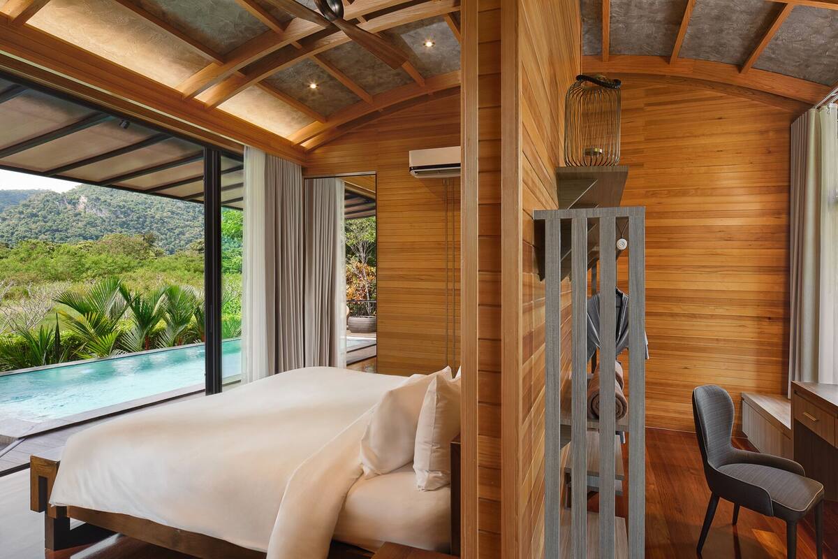 Un dormitorio con una cama grande, un escritorio y vistas a una piscina y zonas verdes.