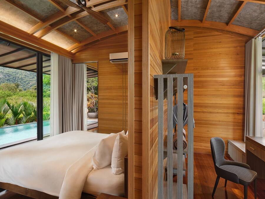 A bedroom with a large bed, a desk, and a view of a pool and greenery.