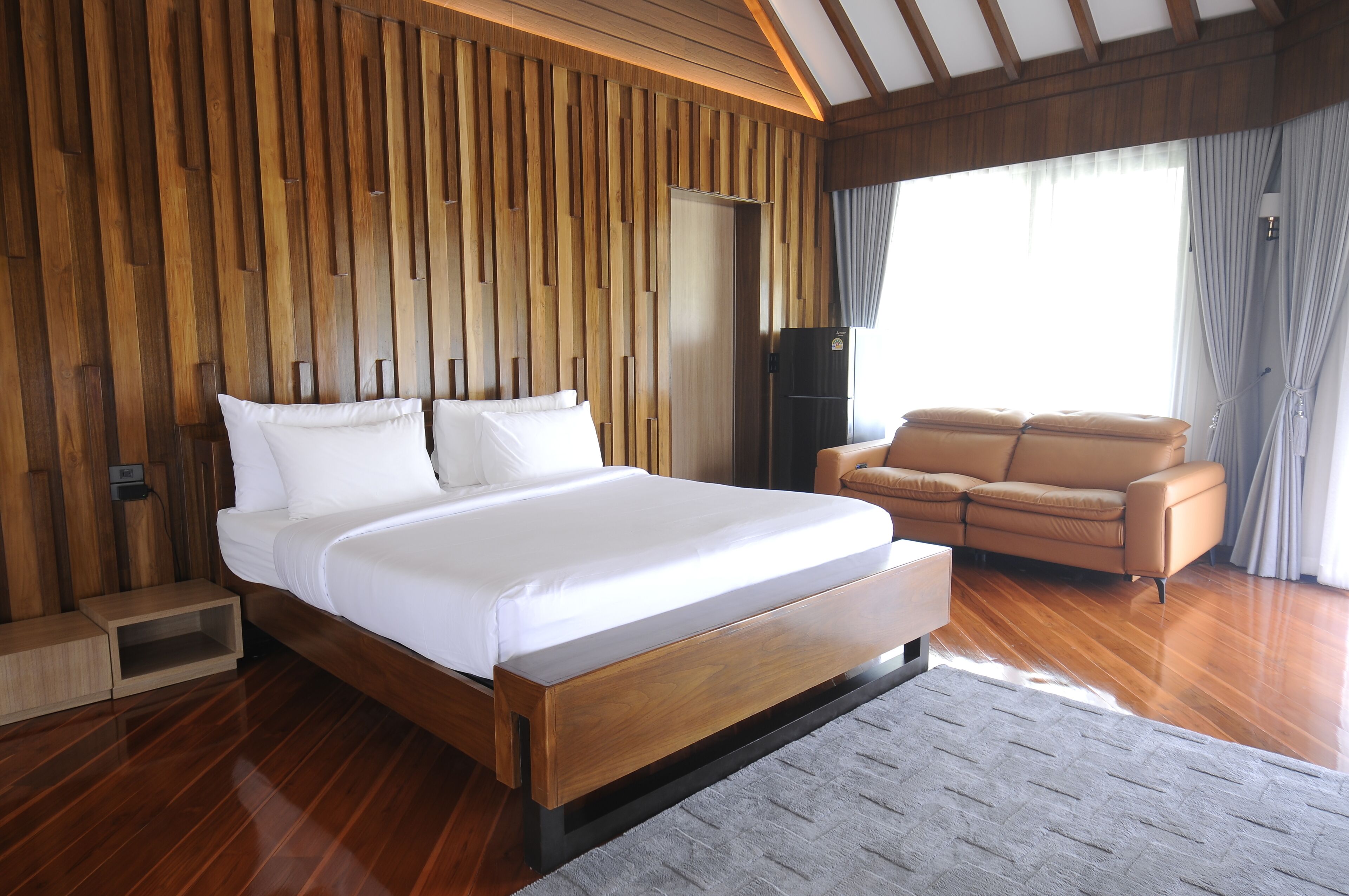 A bedroom with a wooden headboard, a bed with white linens, a sofa, and a wardrobe.