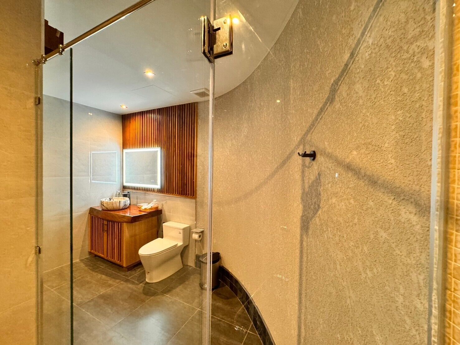 A modern bathroom with a glass shower enclosure, a wooden vanity, and a toilet.