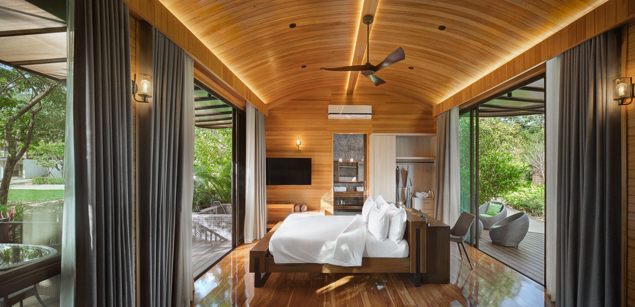A modern bedroom with a wooden ceiling, a bed, a TV, and a view of the outdoors.