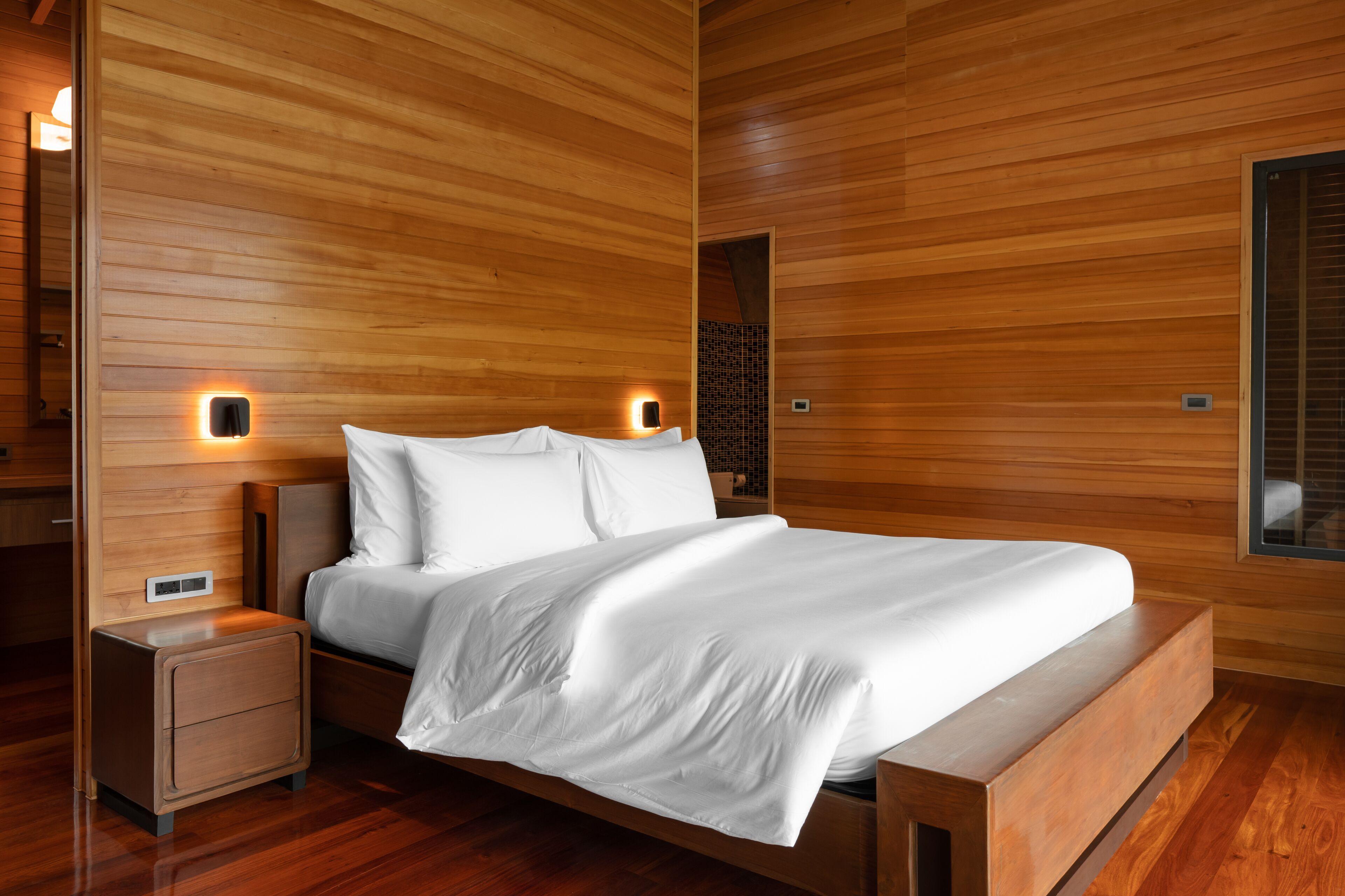Un dormitorio moderno con techo de listones de madera, estructura de cama de madera y dos mesitas de noche con iluminación integrada.