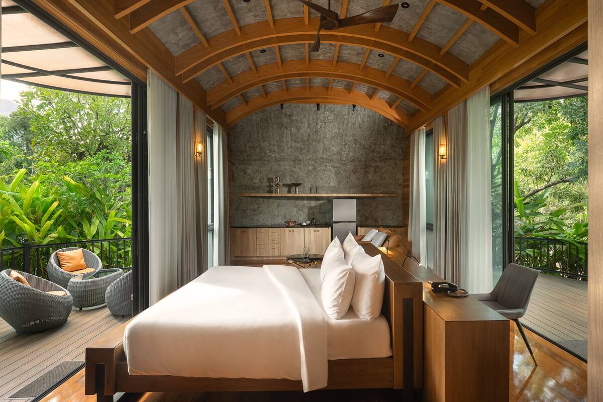 Un dormitorio con una cama grande, un escritorio con una computadora portátil y vistas al exterior.