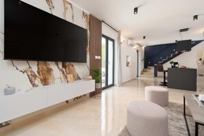 Relax in a spacious living area with a large flat-screen TV, comfortable seating, and a staircase leading to an upper level.