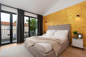Relax in a spacious bedroom with a large bed and tufted headboard, surrounded by a warm textured wall and a sliding glass door leading to a balcony.
