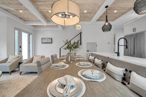Uma sala de estar moderna com teto de madeira, uma área de jantar com uma mesa grande posta para quatro pessoas e uma cozinha com eletrodomésticos de aço inoxidável.