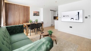 Ein modernes Wohnzimmer mit einem grünen Sofa, einem Essbereich mit Holztisch und -stühlen sowie einer Küche im Hintergrund.