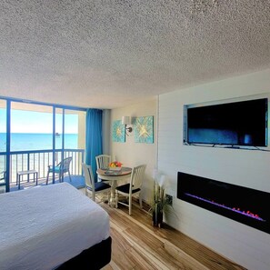 Une chambre d’hôtel avec un lit, une table à manger avec des chaises, un téléviseur fixé au mur et une vue sur l’océan depuis le balcon.