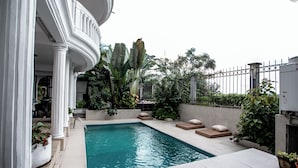 A swimming pool with a tiled deck, surrounded by potted plants and a white column structure. - La Villa des Fées (Douala)