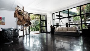 A spacious living room with a black tiled floor, a beige sofa, and a large window offering a view of greenery. - La Villa des Fées (Douala)