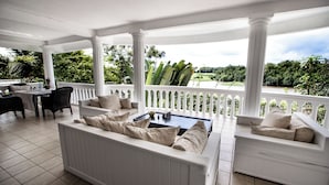 A covered outdoor seating area with white columns, a white sofa, and a dining table. - La Villa des Fées (Douala)