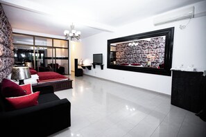 A modern living room with a black sofa, red cushions, a flat-screen TV, a large framed floral artwork, and a chandelier. - La Villa des Fées (Douala)