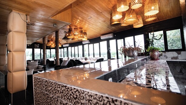 A modern bar area with a marble countertop, leather seating, and large windows offering views of the outdoors. - La Villa des Fées (Douala)