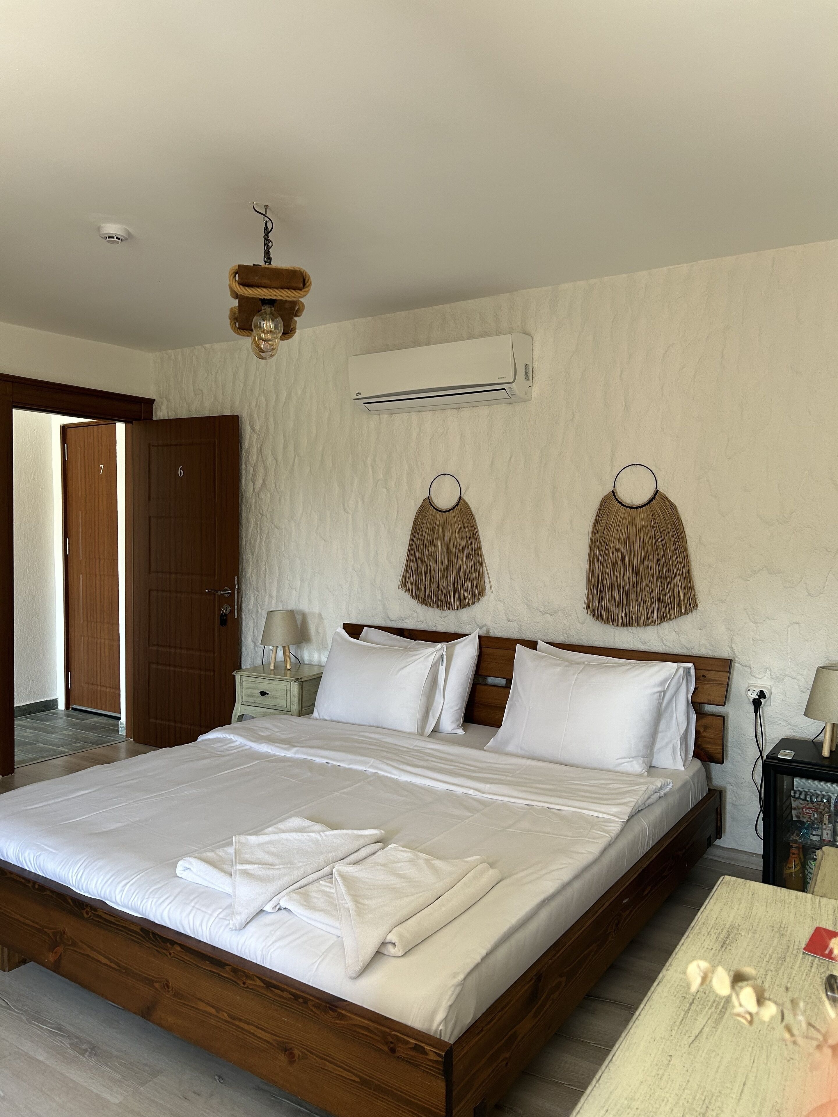 Habitación de hotel con cama de madera, ropa de cama blanca, aire acondicionado instalado en la pared y pared con textura.