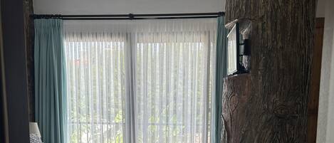 Een slaapkamer met een houten bed, een grote boomstam-zuil, transparante gordijnen en een hanglamp.