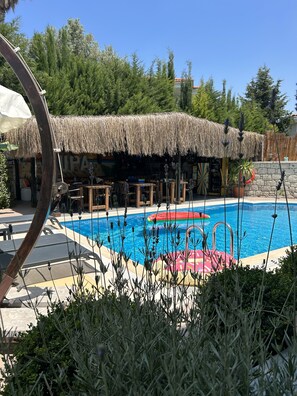 A pool area with a thatched-roof structure, lounge chairs, and a stone wall. - Pupa Alacati Butik Otel (Cesme)